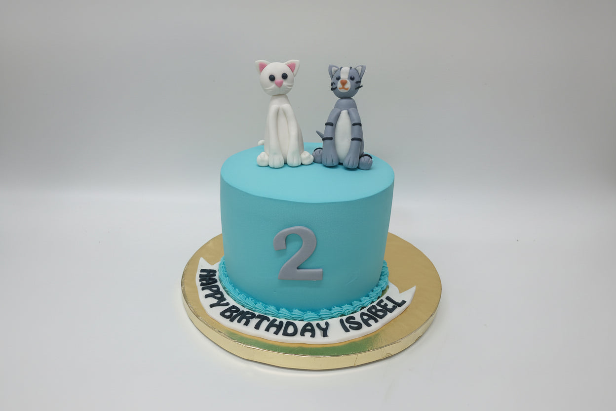 Blue birthday cake with cat figurines on a white background