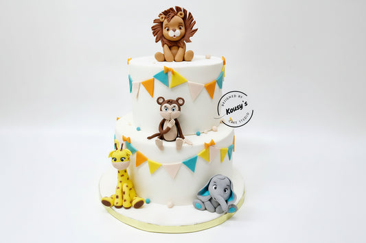 Two-tier cake with animal figurines and colorful flags, designed by Kousy's Cake Studio.