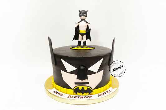 Cake decorated with a Batman theme, featuring a figurine on top, on a white background.