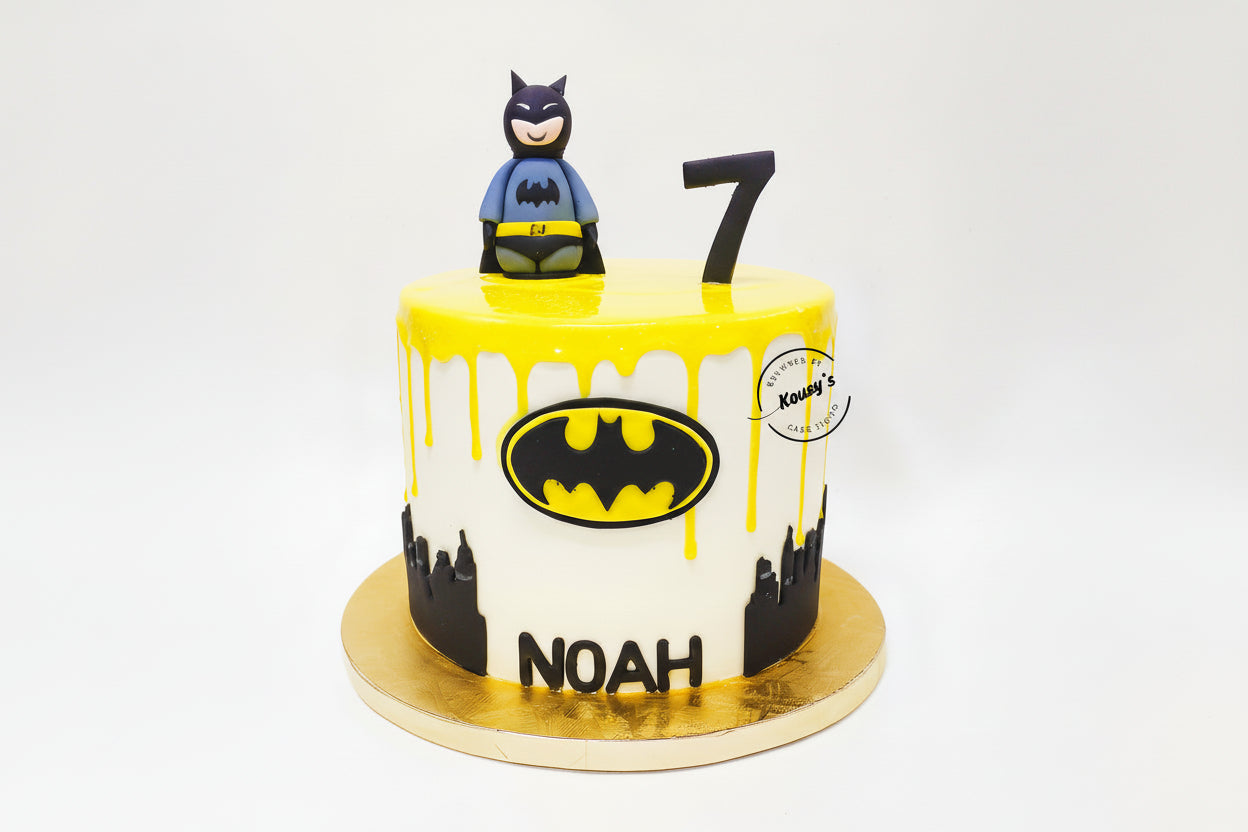 Batman-themed birthday cake with yellow icing, black bat symbol, and number 7 on a white background.