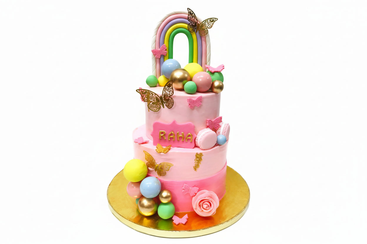 A colorful birthday cake decorated with a rainbow design, butterflies, and sugar balls.