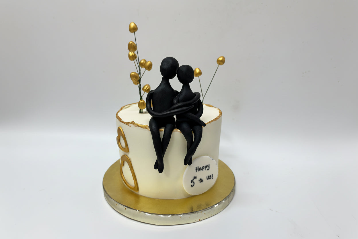 Anniversary cake with black figurines and gold accents on a white background