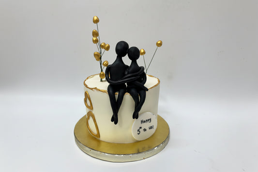 Anniversary cake with black figurines and gold accents on a white background