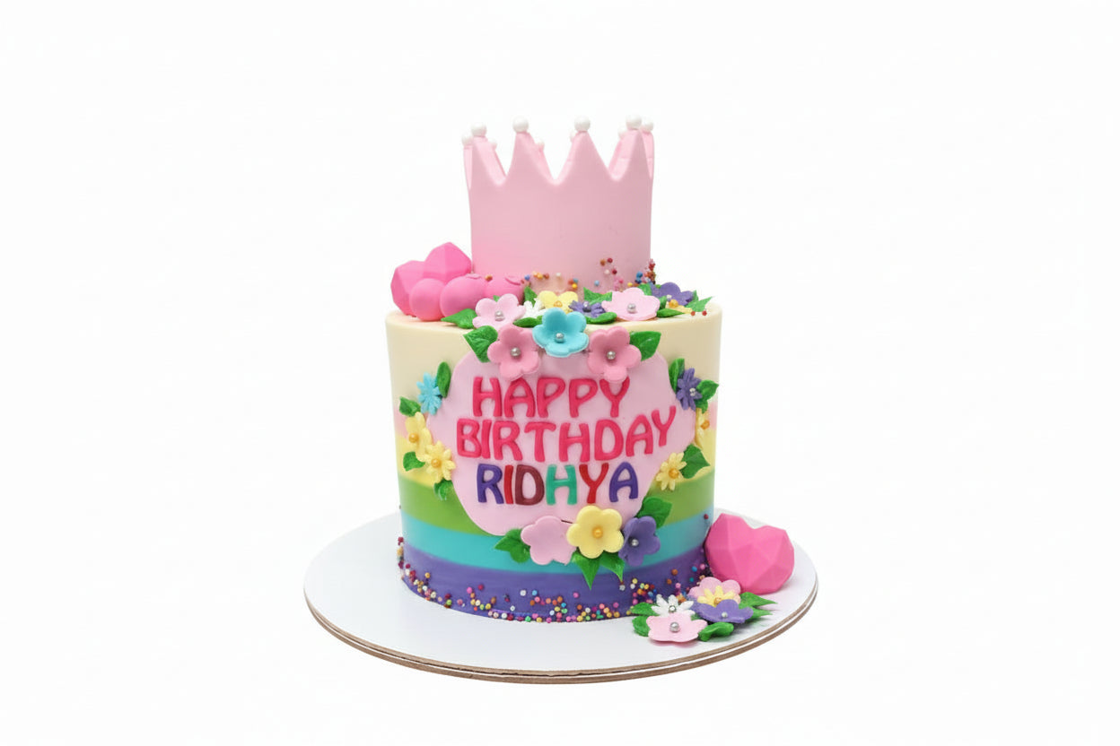 A colorful birthday cake decorated with a princess theme, featuring a pink crown, floral patterns, and the name 'Ridya' on the front.